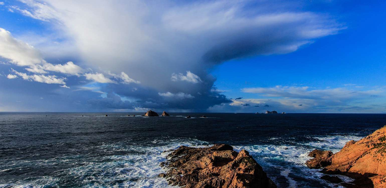 vista das Berlengas com mar e rochas em 1º plano e nuvens dramáticas no céu